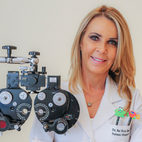 Foto da oftalmologista Ana Tereza. Ela é loira, tem cabelos longos e na foto à frente dela um equipamento oftalmológico.