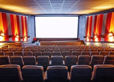 Foto de uma sala de cinema com a tela branca e poltronas vazias.