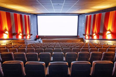 Foto de uma sala de cinema com a tela branca e poltronas vazias.