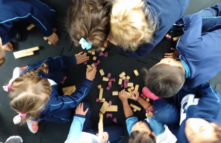 educação: crianças dispostas em círculo brincam com peças de madeira. Foto tirada de cima.