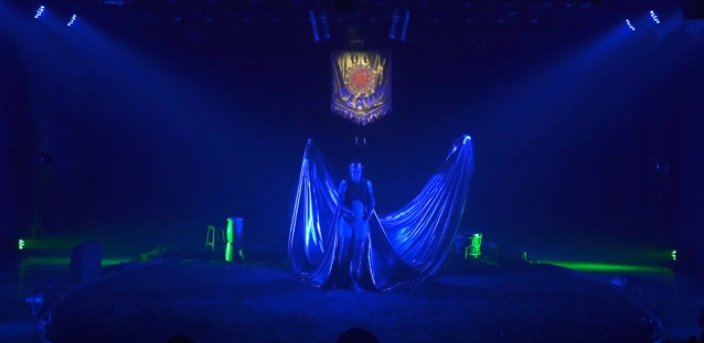 Com uma iluminação na cor azul, uma pessoa em pé com grandes asas.